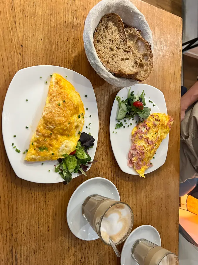 Omelette mit Salat, Brotkorb und zwei Melangen auf einem Holztisch