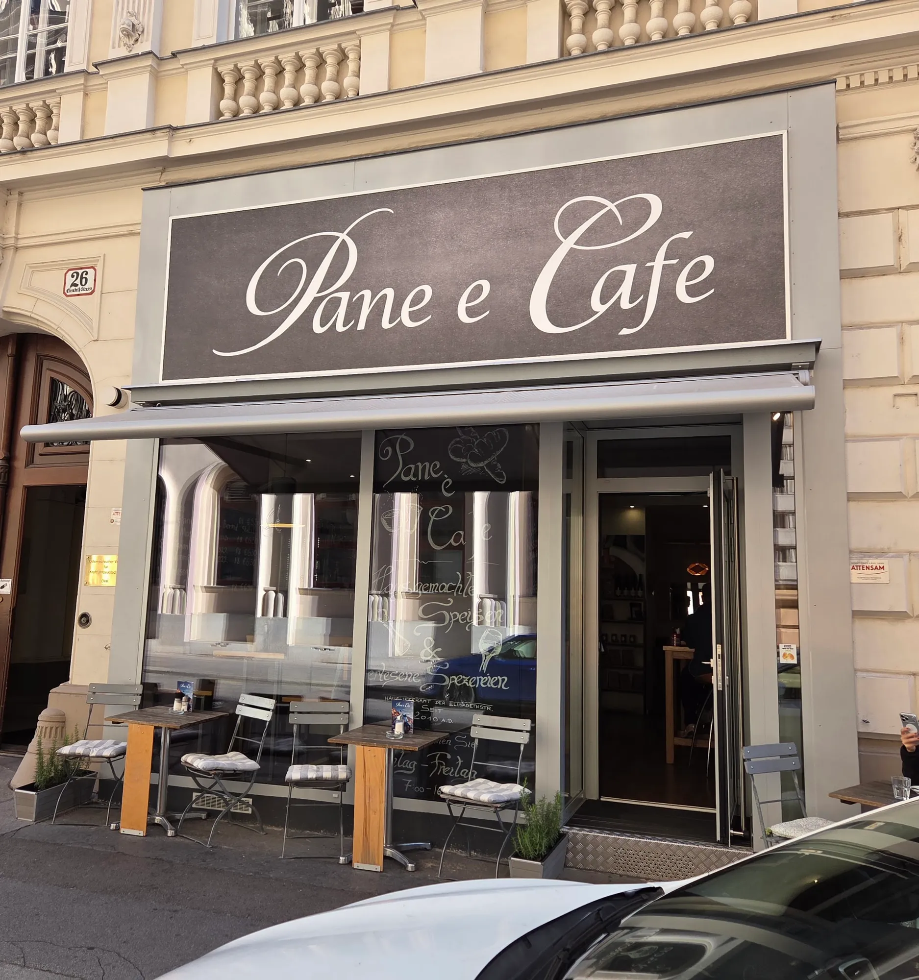 Die Fassade von Pane e Cafe in der Elisabethstraße 26 mit Schriftzug, Markise und Tischen vor der Tür